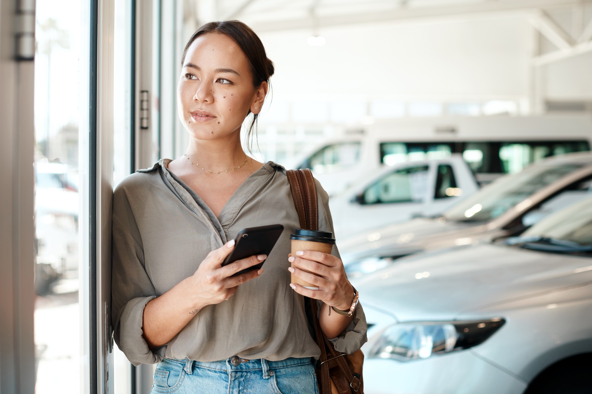 Shot of a young woman using her smartphone in a car dealership